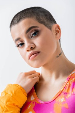 Makyaj ve tarz, kişisel tarz, kısa saçlı dövmeli genç kadının portresi gri arka planda kameraya bakıyor, Z nesli, trend, moda ileri, kadın model, kendini ifade etme 