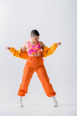 warm clothing, fashionable young woman with short hair posing in puffer jacket and vibrant pants on grey background, outerwear, modern subculture, youthful energy, full length 