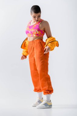youthful energy, fashionable young woman with short hair posing in puffer jacket and vibrant pants on grey background, outerwear, modern subculture, casual wear, full length 