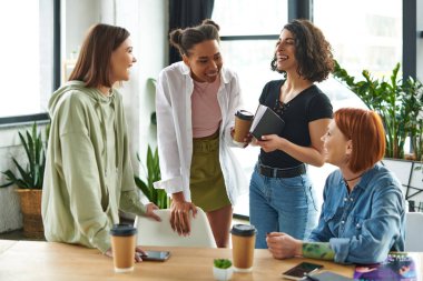 overjoyed multiracial and african american girlfriends with notebook and takeaway drink laughing near positive women in interest club, happy gathering and leisure of diverse female team clipart