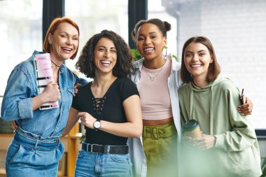 diverse group of stylish and excited multiethnic female friends with coffee to go, smartphone and magazine looking at camera and laughing in women club, mutual support, solidarity and trust concept clipart