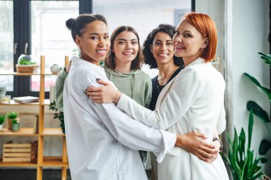 Kızıl saçlı motivasyon koçu olan iyimser ve neşeli çok kültürlü bayan arkadaşlar danışma odasında kameraya sarılıp gülümsüyorlar, kadın birliği ve destek kavramı.