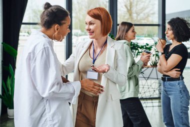 smiling redhead psychologist talking to young african american woman near multiethnic girlfriends drinking coffee to go on blurred background, motivation and supportive therapy concept clipart