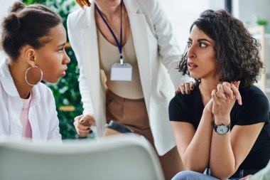 Psikolog, problem çözme ve zihinsel sağIık kavramı ile terapi sırasında genç Afrikalı Amerikalı kız arkadaşının yanında oturan ve ondan uzaklaşan üzgün ve endişeli bir kadın.