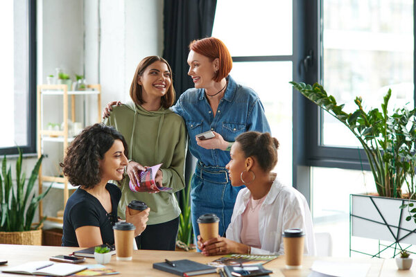 happy redhead woman with smartphone embracing young female friend near multiethnic women drinking coffee to go during conversation n interest club, solidarity and understanding concept