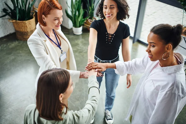 high angle view of multiethnic women and motivation coach joining hands while standing during psychology session, togetherness, moral support and mental wellness concept