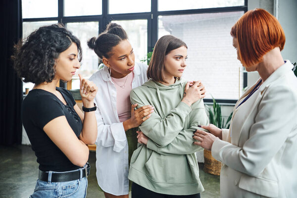 многонациональная женщина успокаивает молодую разочарованную девушку рядом с тренером по мотивации во время сеанса психологии в консультационном зале, концепции решения проблем и психологической помощи
