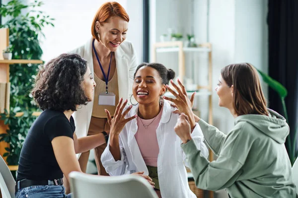 stock image overjoyed african american woman gesturing with closed eyes and talking to multiethnic girlfriends and motivation coach in consulting room, friendship and mental wellness concept
