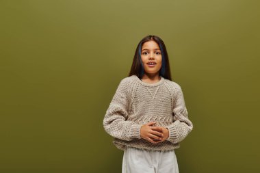 Şık örgü süveter ve gündelik kıyafetlerle boyanmış saçı olan heyecanlı esmer kız kameraya bakarken, gençlik konsepti için çağdaş moda olan yeşil üzerinde tek başına duruyor.