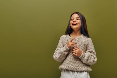 Mutlu ve modaya uygun esmer, saçları boyalı, modern örgü süveter giyen ve gençlik konsepti için çağdaş moda olan yeşil elbisesinin üzerinde tek başına duran genç kız.