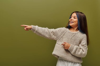 Saçları boyalı, modern örgü süveter giyen ve gençlik konsepti için çağdaş moda olan yeşil, modern modayı işaret eden neşeli ve modaya uygun genç kız.