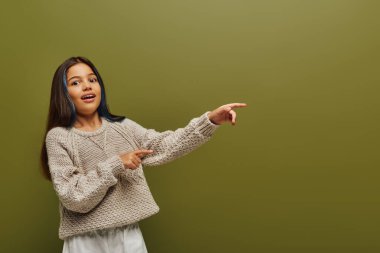 Heyecanlı ve şık, boyalı saçlı, örgü kazak giyen ve kameraya bakarken yeşil, çağdaş moda konsepti için parmakları izole edilmiş genç kız.