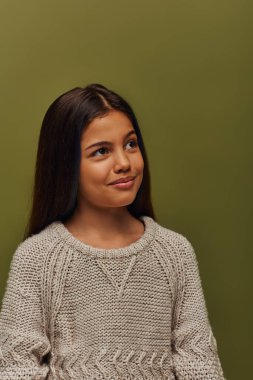 Düşünceli ve şık esmer genç kız portresi örgü kazak giymiş yeşil, şık sonbahar kıyafetleri içinde yalnız poz verirken ve dikilirken başka tarafa bakıyor.