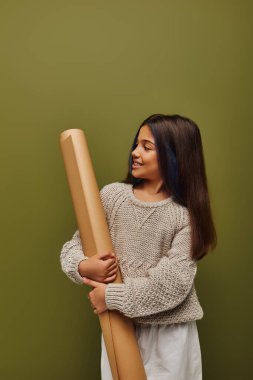 Saçları boyalı, şık ve rahat sonbahar örgü süveteri giyen, yuvarlak kağıda bakan ve yeşil üzerine izole edilmiş, sonbahar titreşimleri saçan neşeli ergen kız.