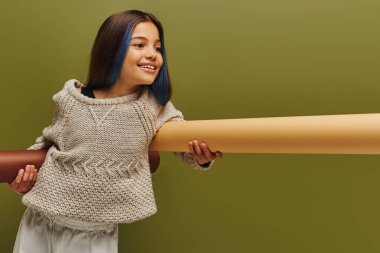 Gülümseyen ve modaya uygun, boyalı saçlı, güzel örgü süveterli, sarılı kağıtları tutan ve gençlik konsepti için yeşil, sonbahar modasından soyutlanmış genç kız.
