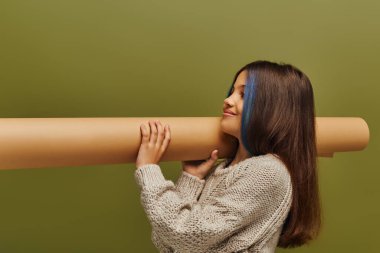 Gülümseyen, boyalı saçlı, örgü kazaklı, rulo kağıtlı genç kız yeşil, sonbahar modasında gençlerin konsepti için tek başına dikilirken.