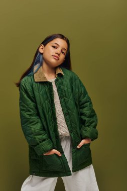 Kendine güvenen, esmer, boyalı saçlı, sonbahar kıyafetiyle poz veren, süveter ören ve gençlik konsepti için modern sonbahar modasında izole edilmiş kameraya bakan genç kız.