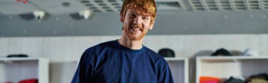 Portrait of young redhead craftsman in casual clothes looking at camera while standing in blurred print studio at background, self-made success concept, banner  clipart