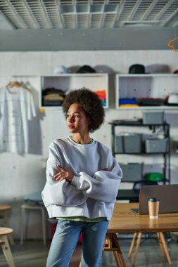 Tişört ve kot pantolon giyen kendine güvenen Afro-Amerikalı bir kadın. Bulanık baskı stüdyosunda duruyor, atölyede hevesli bir iş adamı.
