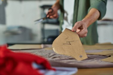 Bulanık baskı stüdyosundaki kumaşın yanında dikiş deseni ve makas tutan bulanık genç zanaatkârın görüntüsü. Birden fazla projeyi yöneten çok iş sahibi.