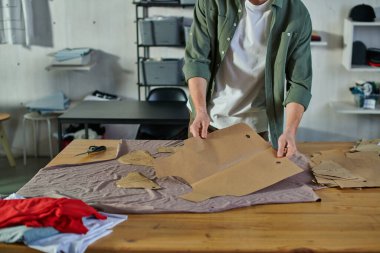 Bulanık baskı stüdyosundaki masanın üzerinde dikiş desenleri tutan genç zanaatkârın görüntüsü. Birden fazla projeyi yöneten çoklu iş sahibi.