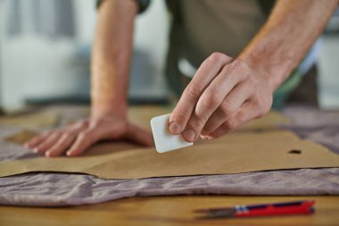 Arka plandaki baskı stüdyosunda dikiş desenleri olan kumaşın yanında boya kalemi tutan bulanık bir zanaatkarın görüntüsü, birden fazla projeyi yöneten çoklu iş sahibi.