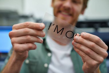 Cropped view of young blurred craftsman holding printing layer with I'm ok lettering in print studio, small business owner working on project, close up, creative process, workflow  clipart