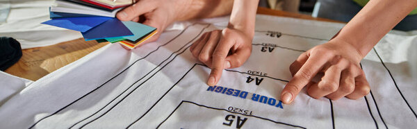 Cropped view of african american designer holding printing layer on t-shirt on table near colleague with color swatches in print studio, thriving small enterprise concept, banner 