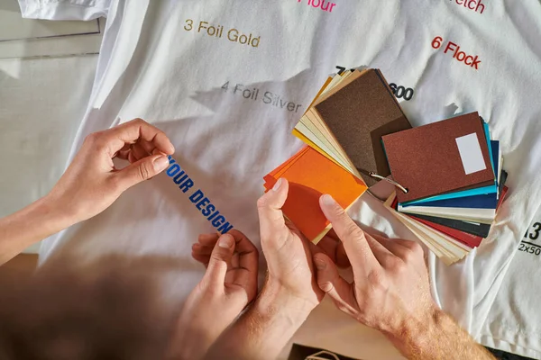 stock image Top view of young craftsman pointing at color swatches while working with african american colleague, clothes and printing layer in print studio, self-employment opportunity concept