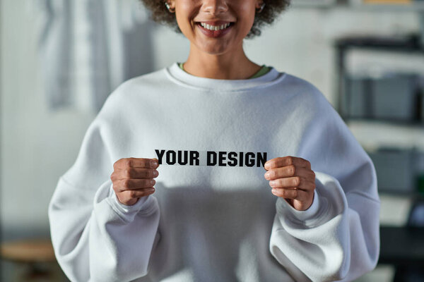 Cropped view of smiling young african american craftswoman holding printing layer with your design lettering and standing in print studio, focused business owner managing workshop