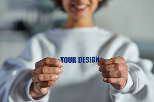 Cropped view of blurred and cheerful young african american artisan in sweatshirt holding printing layer with your design lettering in print studio, focused business owner managing workshop