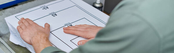 Обрезанный вид молодого ремесленника, держащего футболку с маркировкой рядом с экранной печатью в типографии, ориентированная на клиента концепция малого бизнеса, креативность, баннер 