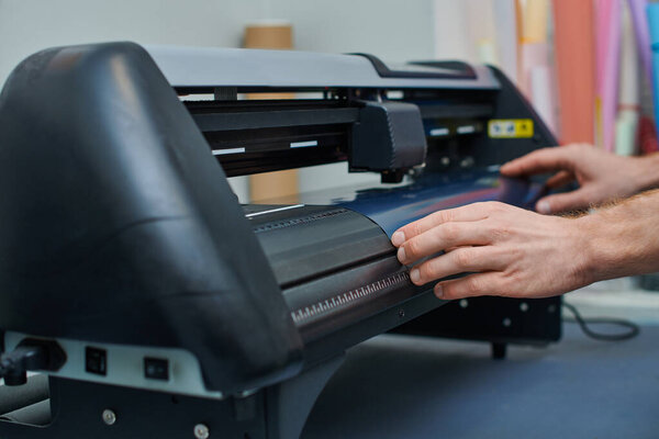 Cropped view of young craftsman holding layer near screen printing machine while working in print studio, small business owner working on project, creativity 