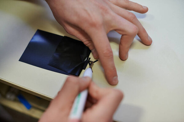 Cropped view of young craftsman working with tool and layer for screen printing in print studio, small business owner working on project, close up, creative process, workflow 