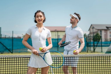Çalışan mutlu kadın tenis raketini erkeğin yanında tutuyor, tenis oyuncuları kortta.