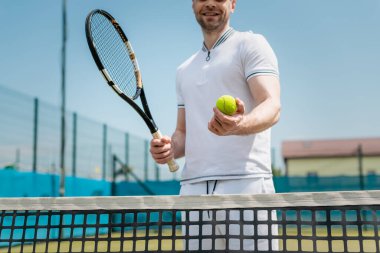 Spor kıyafetleri içinde tenis raketi ve topu kalenin, oyuncunun, hobisinin ve sporun yanında tutan adam görüntüsü.