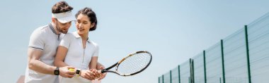 banner, cheerful man teaching girlfriend how to play tennis on court, holding rackets and ball clipart