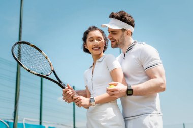 Yaz aşkı ve spor, afiş, neşeli adam kız arkadaşına kortta tenis oynamayı öğretiyor.