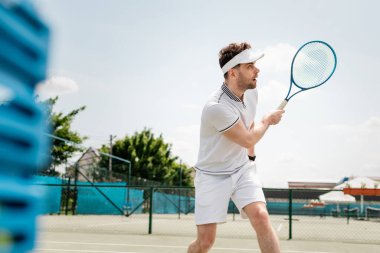 Spor vizöründe yakışıklı bir tenisçi raket tutuyor ve kortta tenis oynuyor.