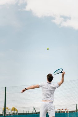 Sahada tenis oynayan, raket tutan, topa vuran, ters vuruş yapan bir adam.