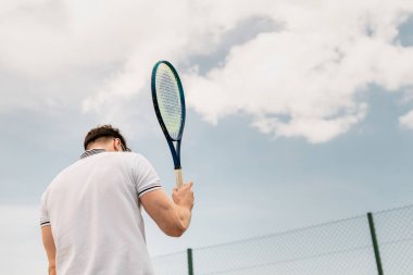 back view of sportive man holding tennis racket on court against sky, motivation, sport clipart
