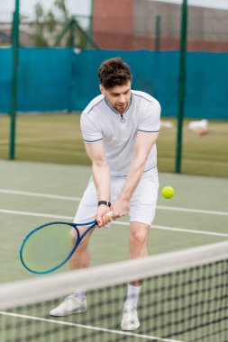 Yakışıklı tenisçi raket tutuyor ve kortta tenis topuna vuruyor, hobi olarak spor yapıyor.