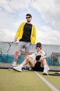 couple sport, man and woman in sunglasses posing near tennis net with rackets, sporty fashion clipart