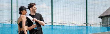 Pankart, aktif görevde olan mutlu çift tenis kortunda havlu ve spor şişesiyle ayakta duruyor.