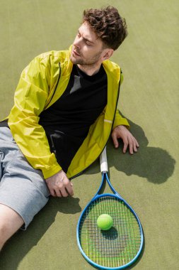 Üstten atış, tenis topu ve raketin yanında dinlenen yakışıklı adam, korttaki erkek tenisçi.