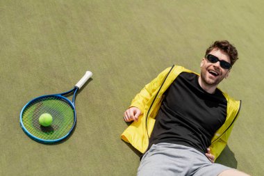 happy man in sunglasses resting near tennis ball and racquet, male tennis player, sport and style clipart