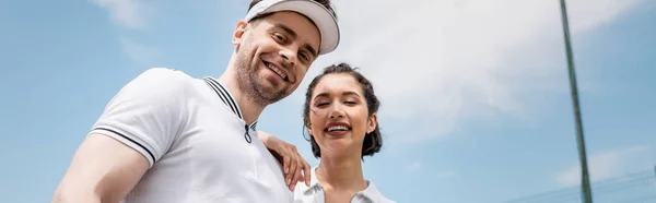 Stock image banner, cheerful couple in active wear looking at camera on tennis court, hobby and sport