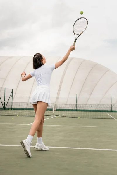 motivation and sport, back view of sportswoman hitting the ball while playing tennis on court