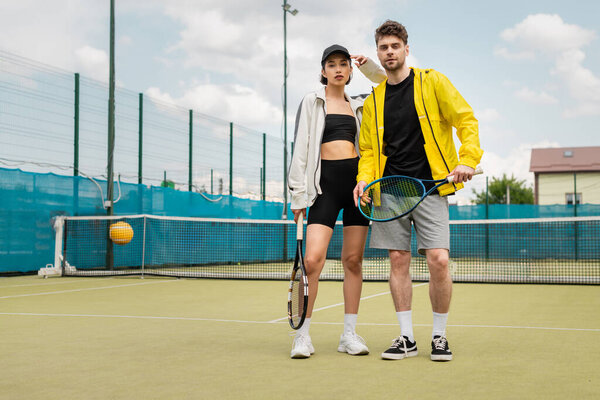 fashionable couple standing on tennis court with rackets, man and woman in sportswear, players