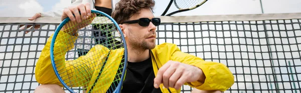 banner, man in sunglasses and active wear holding racket near woman and tennis net, sporty fashion